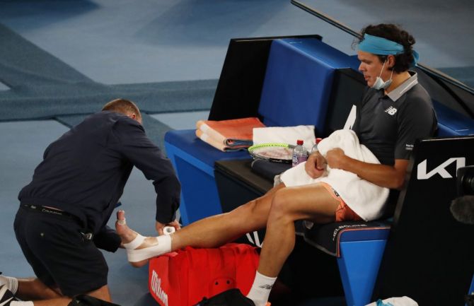 Milos Raonic receives medical attention during his fourth round match against Novak Djokovic