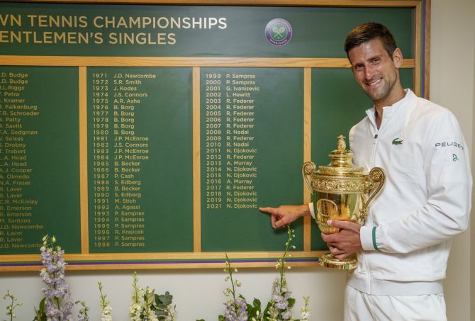 Serbia's Novak Djokovic celebrates with the trophy in front of the honours board and points to his name