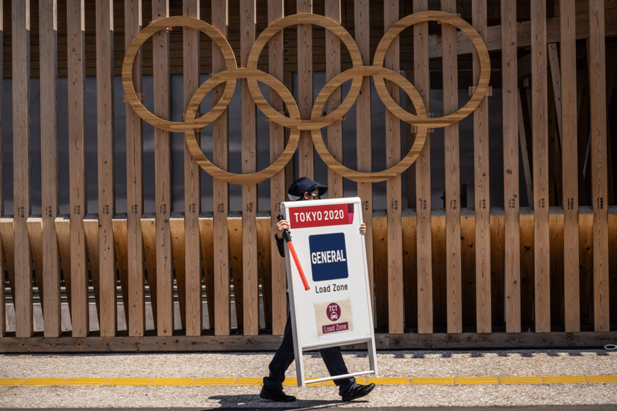 A security guard carries a sign past Olympic Rings near the Tokyo Olympics athletes village on Monday