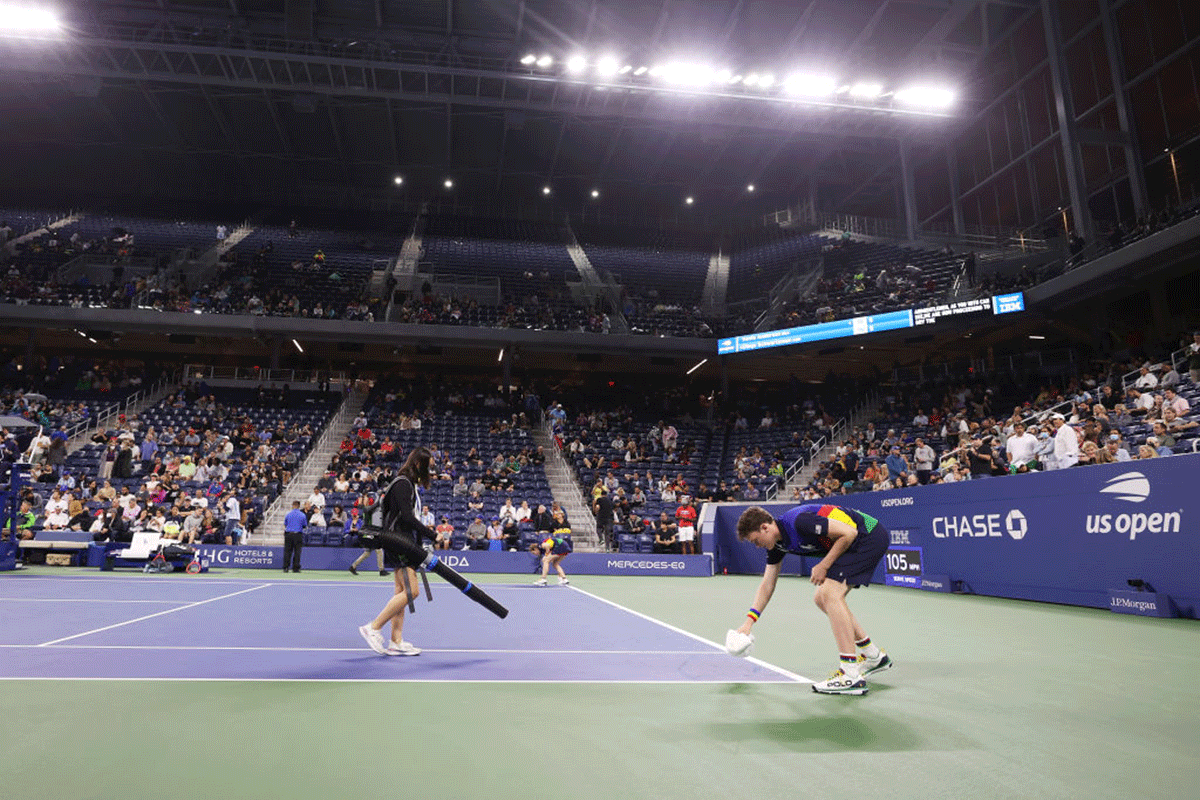 Volunteers dry the court after rain enters through the outer openings of the roof causing a delay during the match between Kevin Anderson and Diego Schwartzman on Wednesday