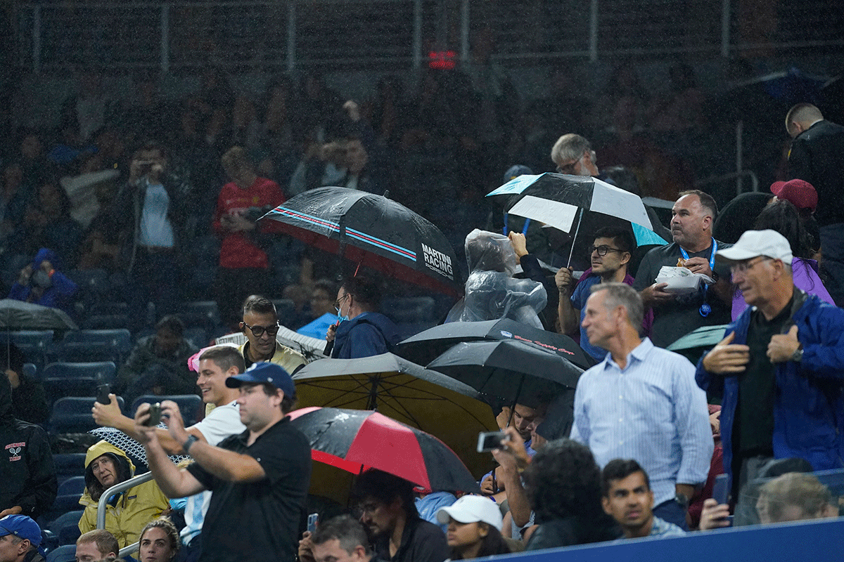 Spectators open their umbrellas as rain falls into Louis Armstrong Stadium during the second round match between Diego Schwartzman and Kevin Anderson on day three of the 2021 US Open tennis tournament at USTA Billie Jean King National Tennis Center on Wednesday
