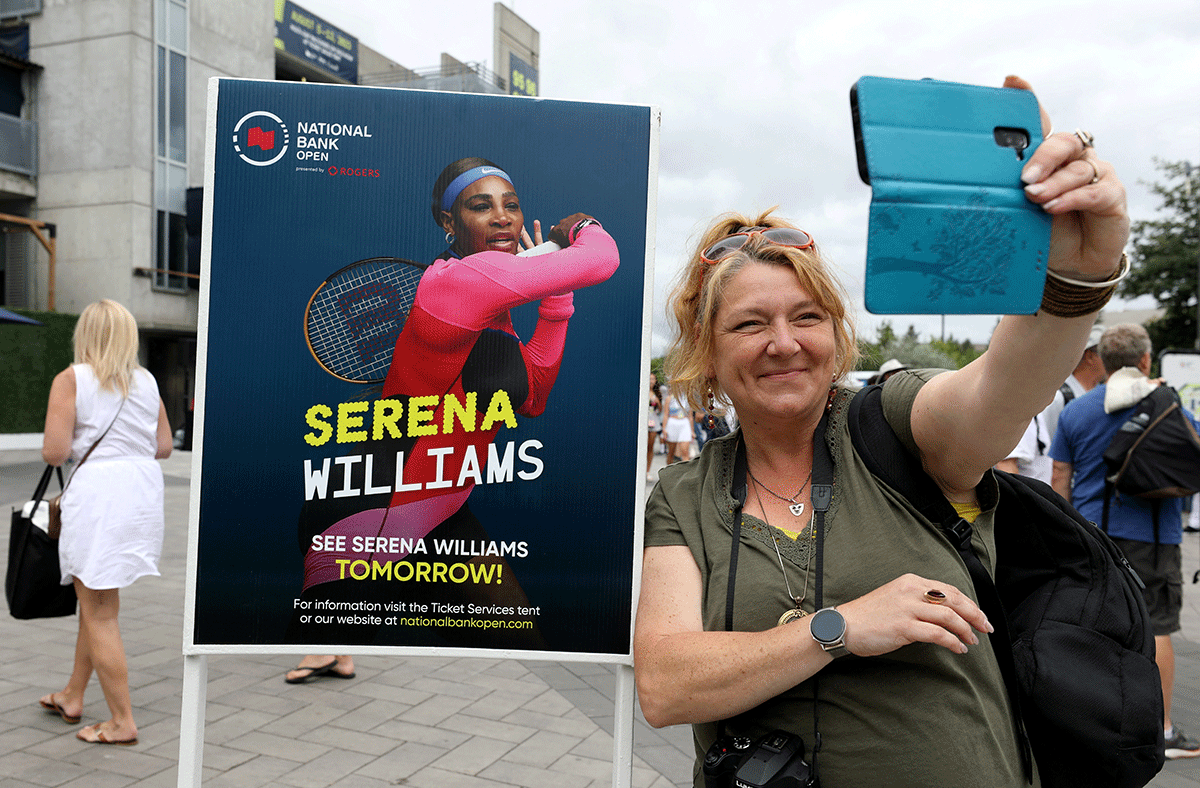 A woman takes a selfie with a poster advertising the match of veteran tennis player Serena Williams outside a stadium at the National Bank Open in Toronto, Ontario, Canada, on Tuesday