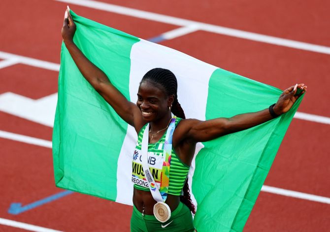 Tobi Amusan celebrates with the flag of Nigeria after medal ceremony