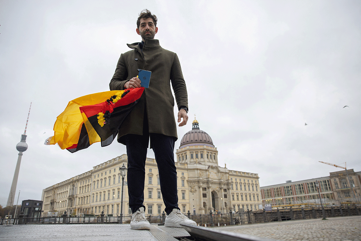Hani Z., a refugee from Syria living in Germany, poses with his travel document and fan merchandise in the colours of Germany's flag in Berlin, Germany. He was denied a visa by Qatar to travel to the FIFA World Cup 