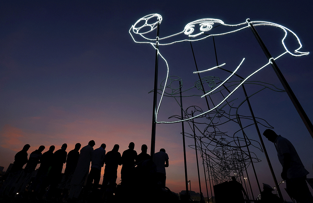 Believers pray at sunset next to the illuminated FIFA World Cup Qatar 2022 mascot La'eeb, in Doha, Qatar