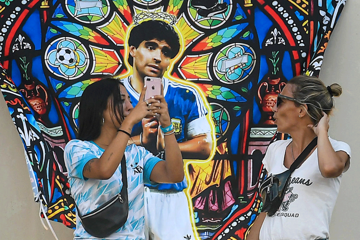 Fans of Argentina talk next to a graffiti of late football legend Diego Maradona before the FIFA World Cup qualifier at Mario Alberto Kempes Stadium in Cordoba, Argentina, on February 1