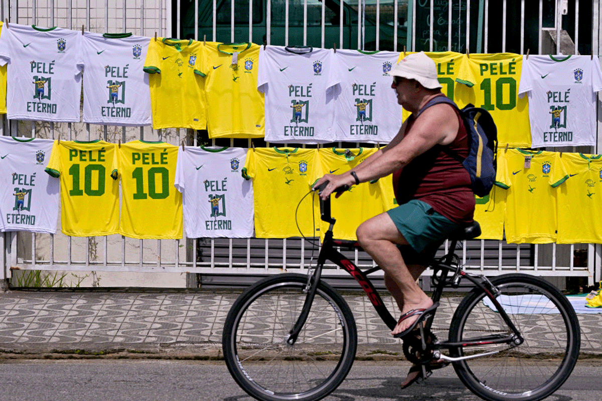 Un hombre pasa en bicicleta frente a una camiseta de Pele a la venta durante su funeral en el estadio de Vila Belmiro.