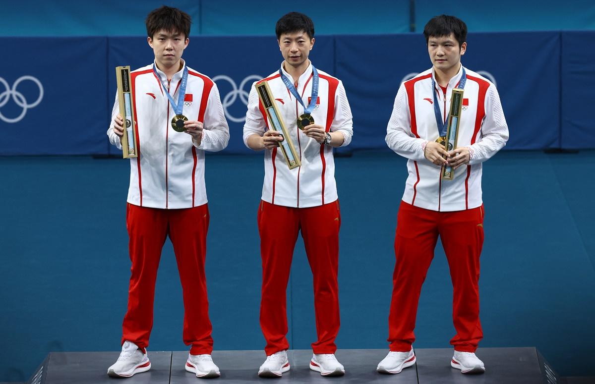 China's men's Table Tennis gold medal-winning team of Ma Long, Chuqin Wang and Zhendong Fan celebrate with their medals on the podium.