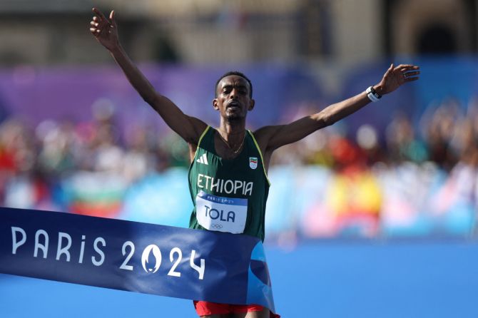 Ethiopia's  Tamirat Tola celebrates as he crosses the finish line at Invalides to win gold in the Men's Marathon at the Paris Olympics, on Saturday.