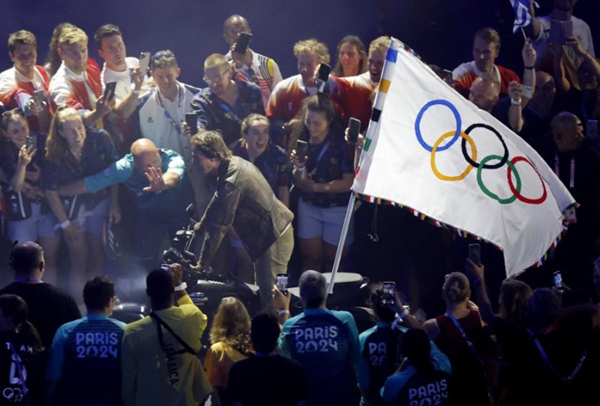 Tom Cruise retuns on a motorcycle with the Olympic flag affixed to the back and rides through the stadium.