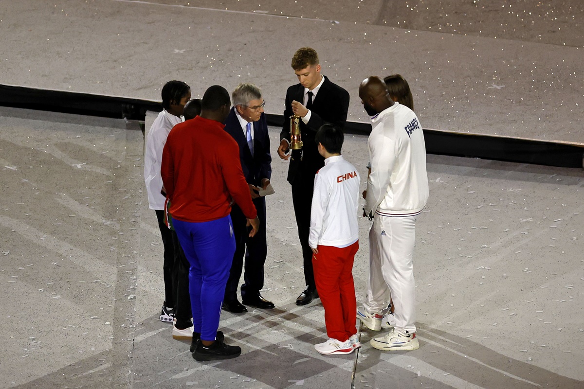 Leon Marchand, IOC president Thomas Bach and fellow Olympians get ready to put off Olympic flame. 