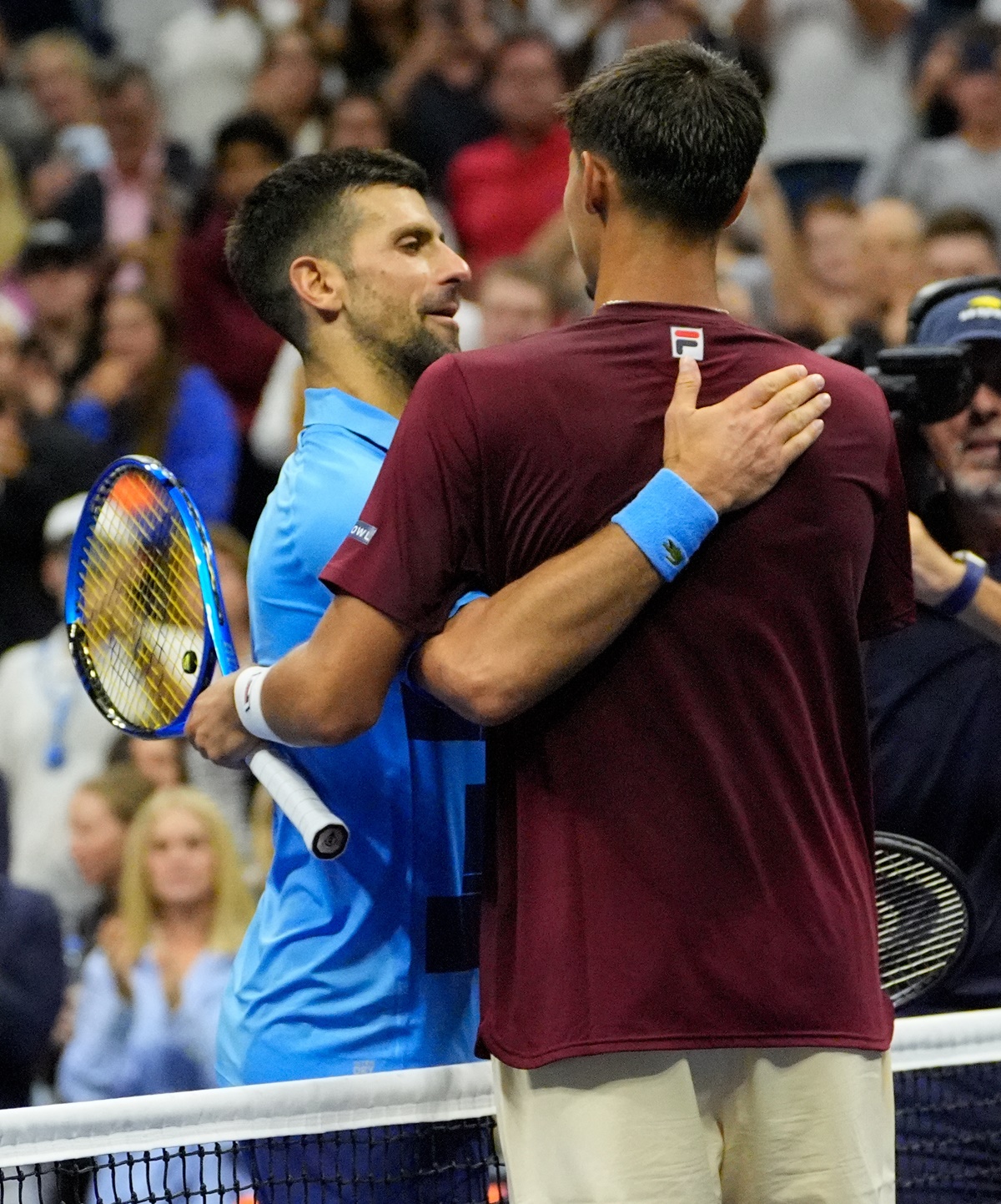 Alexei Popyrin and Novak Djokovic embrace after the match at the net.