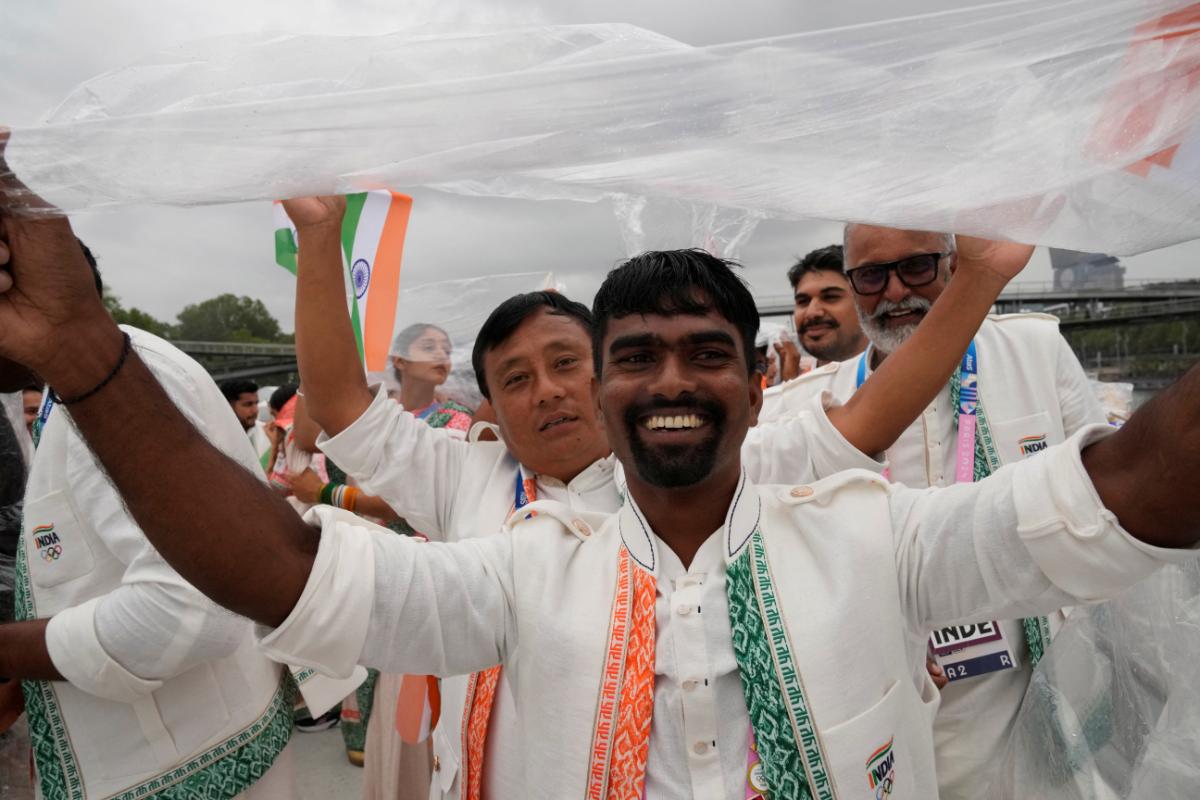 Indian athletes use a plastic sheet to shelter themselves from rain as they travel in a boat on the Seine River during the opening ceremony of the 2024 Summer Olympic