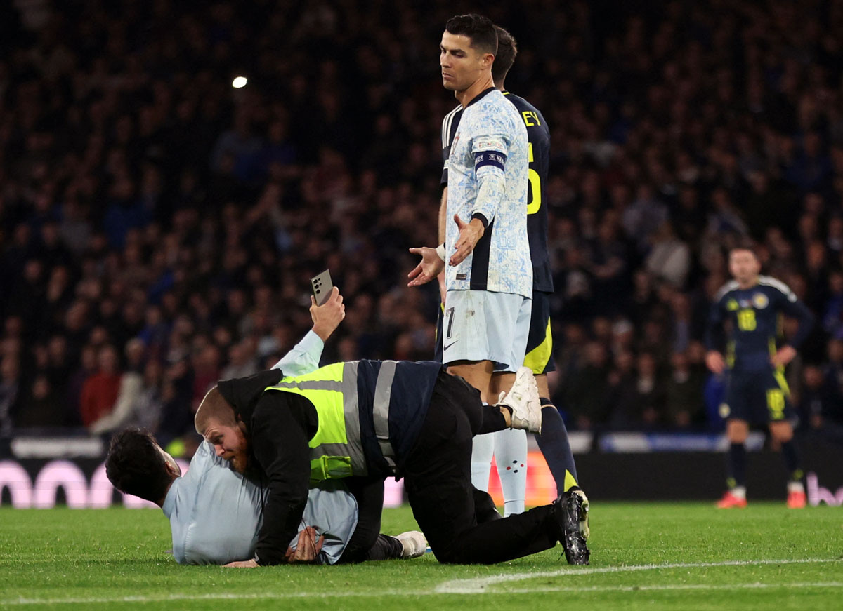 A steward tackles a pitch invader as Cristiano Ronaldo reacts