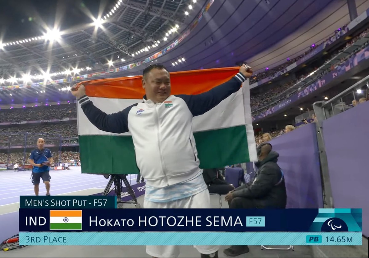 Hokato Hotozhe Sema celebrates with the national flag after attaining his personal best of 14.65 metres.