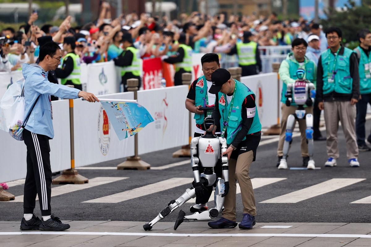 An engineer supports a humanoid robot after it falls at the starting line.