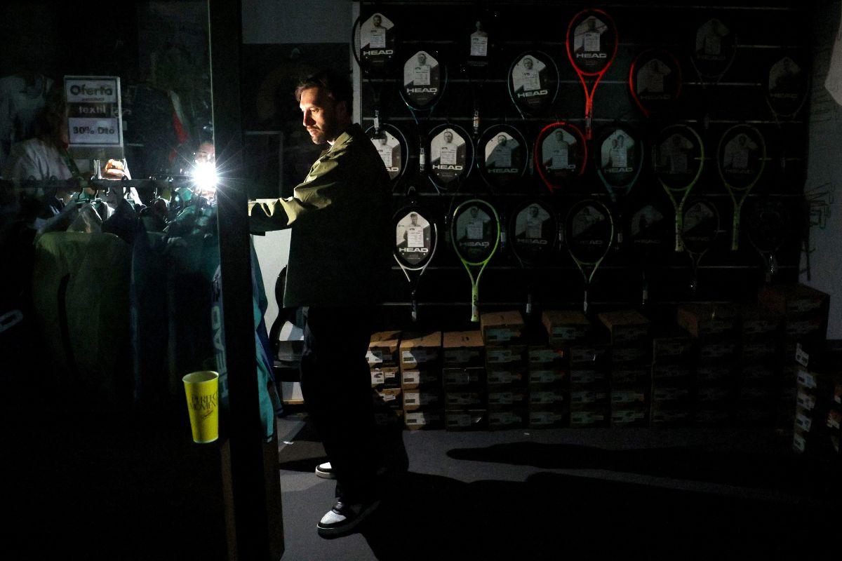 A man uses his cell phone's flashlight in a dark sports shop after the matches get suspended due to a power outage