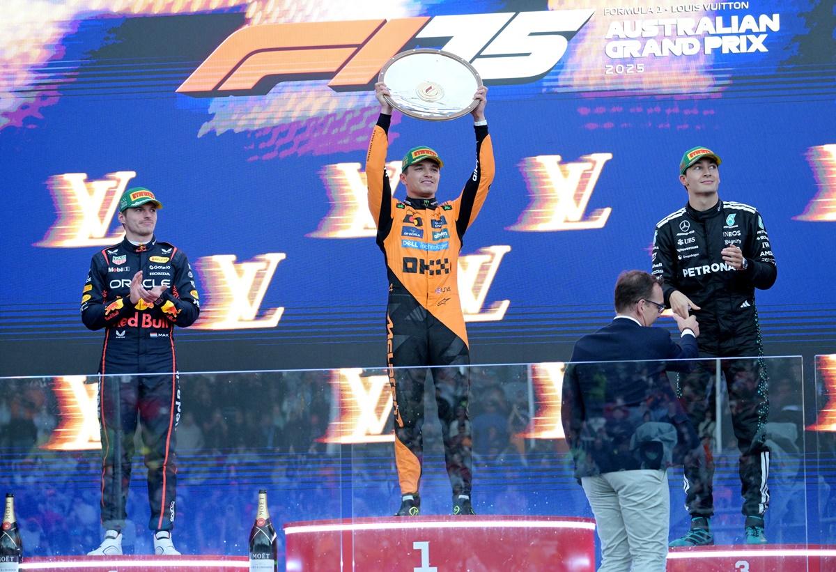 Lando Norris celebrates with the trophy on the podium with second-placed Red Bull's Max Verstappen and third-placed George Russell of Mercedes.