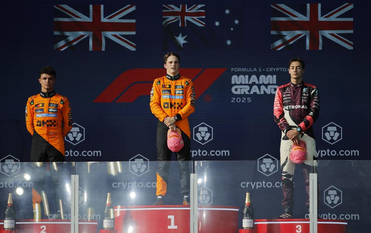 McLaren's Oscar Piastri stands on the podium alongside second placed teammate Lando Norris and third placed Mercedes's George Russell.