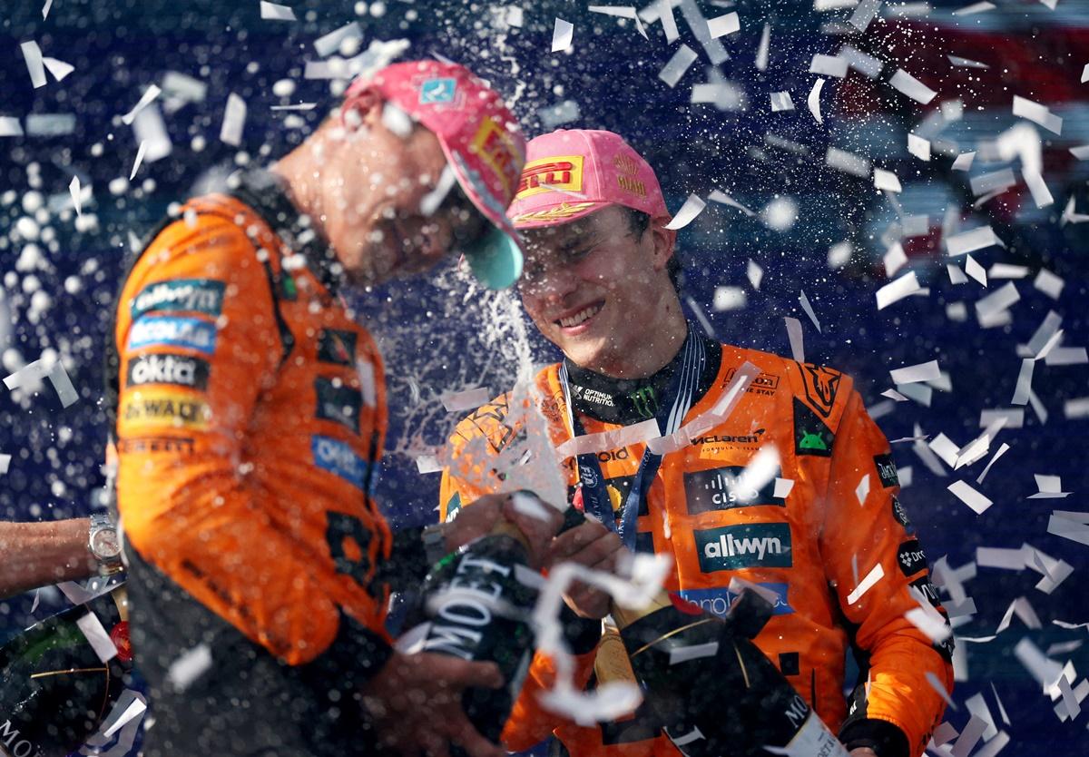 Oscar Piastri celebrates with champagne on the podium alongside Lando Norris.